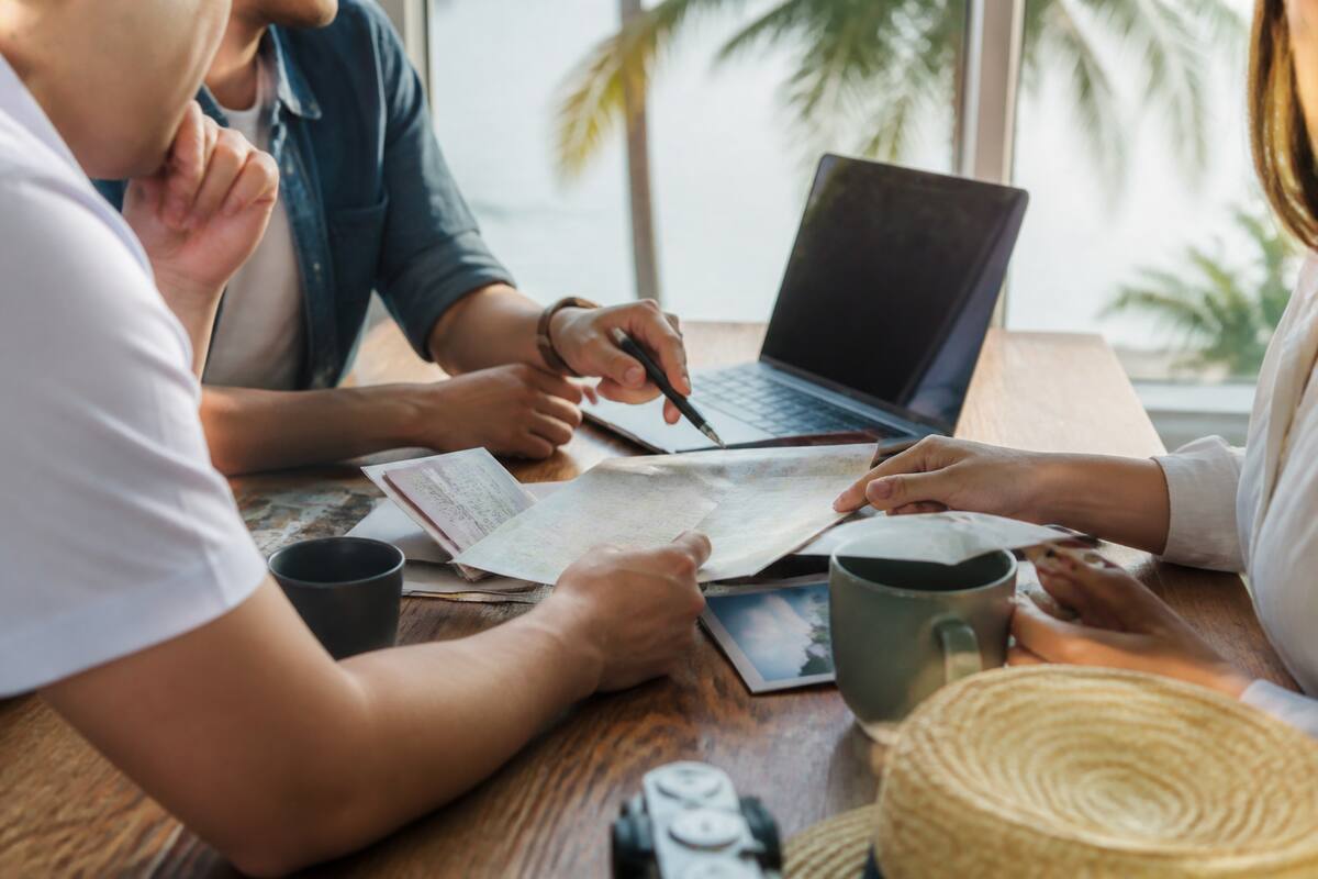 Reizigers vergelijken vakanties op een laptop aan tafel met reisdocumenten en reisplannen