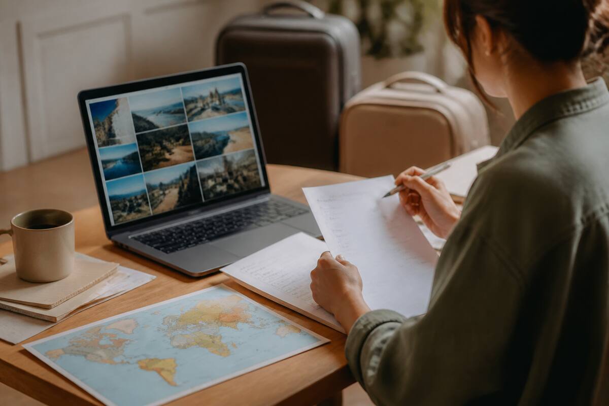 Iemand vergelijkt vakantieopties op laptop met notities en koffiemok op tafel